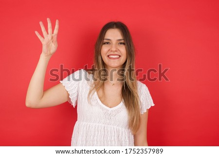 Young   woman standing against gray wall showing and pointing up with fingers number four while smiling confident and happy.