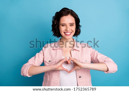 Photo of beautiful cheerful funny lady short black hairdo hold arms making heart figure shape dreamer express feelings wear casual pink jacket isolated blue color background