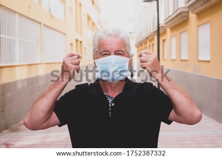 portrait and close up of one senior and mature man taking off his medical and surgical mask after coronavirus - freedom lifestyle and concept