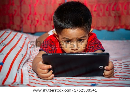 A child with full attention on his bed watching cartoons using the Tab smartphone. Kids playing with smartphone. Mobile phone and internet addiction concept.