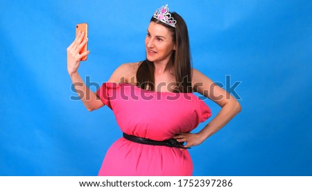 The most beautiful girl in a pink dress from pillows makes a selfie on a blue background. Crazy quarantine. Fashion 2020. Put on a pillow. Challenge 2020 due to house isolation.
