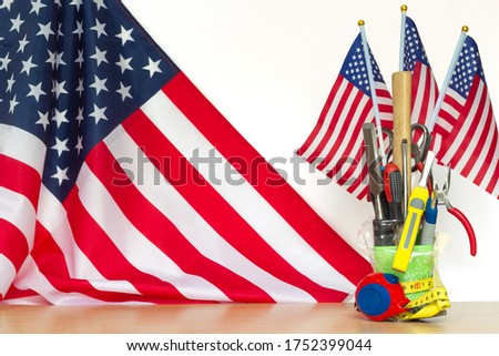 Bouquet of tools with small US flags on a table and big US flag on white background, concept of the labor day holiday