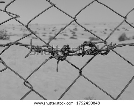 Rusted metal fence with barbed wire in arid Arabian desert sand dunes. Black and white.