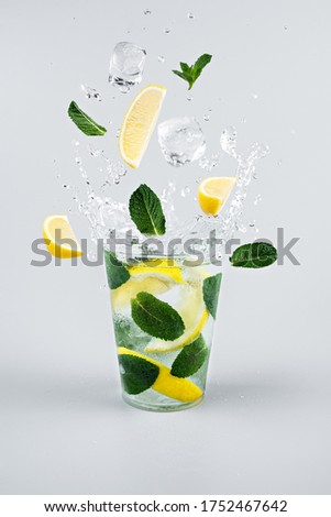 Ice cubes, slices of lemon and mint leaves splashing into glass of lemonade. Light grey background Royalty-Free Stock Photo #1752467642
