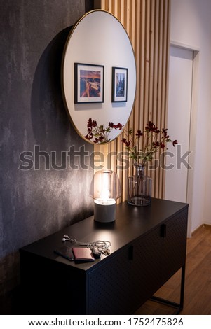 Hallway with a golden mirror in front of a wooden wall and grey decor. Black metal chest with a warm light and flowers