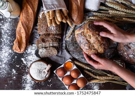 Concept of homemade bread, natural farm products, domestic production. Healthy and tasty organic food. Woman baked round whole grain bread. Top view flat lay, dark black background. 