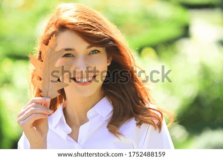 Cheerful smiling ginger woman holding fall oak leaves. Healthy and natural woman beauty. Happy smiling girl with natural red hair. Autumn woman with bright orange hair