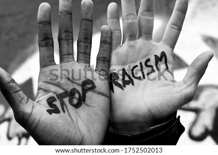 Close-up of the raised hands of two men of different ethnicity with the slogan "stop racism" written on their palms. Black and white anti racism image. Royalty-Free Stock Photo #1752502013