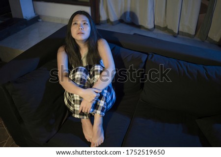 dramatic home lifestyle portrait of young beautiful sad and depressed Asian Chinese woman lying in pain crying at living room sofa couch feeling stressed and worried suffering depression 