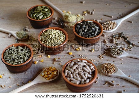 Different kinds of pelleted compound feed in bowls and spoons on wood table, copy space Royalty-Free Stock Photo #1752520631