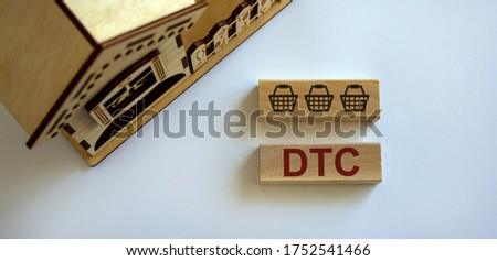 Wooden block form the word 'DTC' and food basket icon near miniature house. Beautiful white background, copy space. Home delivery concept.