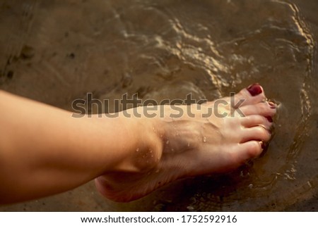Female feet barefoot on a sandy beach in the water. Close-up of beautiful female legs. Wet foot.