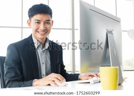 Portrait of Asian smiling confident business man working with computer at office desk in consult or financial banking company. success businessman learning startup project
