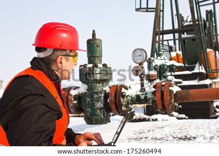 worker on an oil pump looks to manometer,best focus helmet and glasses,pump soft focus