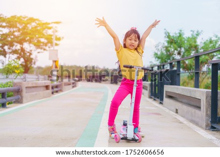 Little child girl to ride scooter in outdoor sports ground on sunny summer day. Active leisure and outdoor sport for children.