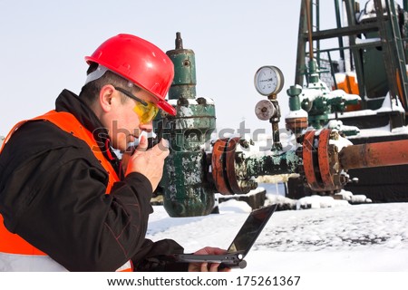 worker on an oil pump looks at laptop and speaking in a radio station,best focus Slam, right hand, laptop, glasses,Soft focus manometer,pump