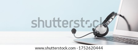 Part of Laptop with blank screen with headphones on desk blue background. copy space. Distant learning or working from home, online courses. Helpdesk or call center headset minima concept banner Royalty-Free Stock Photo #1752620444