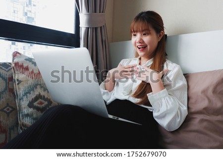 Image of an asian woman with a surprise face while looking at a laptop screen. Background of a bedroom.
