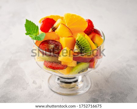 Fruit salad with mango, strawberries, kiwi, peach in a glass bowl.