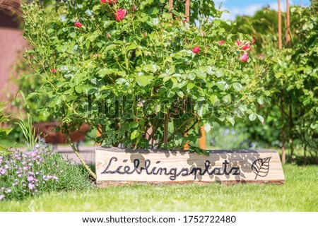 Blooming flowers in the green garden with a wooden sign and the inscription Favorite place in german language
