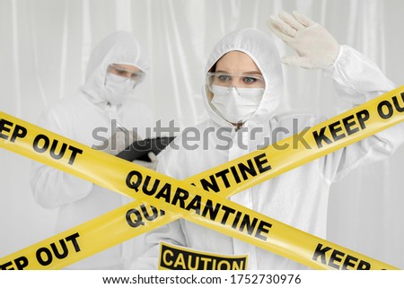 Epidemiologists a man and a woman in protective clothing are in a restricted area with a danger sign. Yellow line Keep Out Quarantine. Quarantine alert sign. Coronavirus, covid-19.