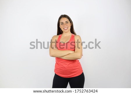 young pretty girl wearing a sport T-shirt standing on an isolated white background and happy face smiling with folded arms looking at the camera. Positive person.
