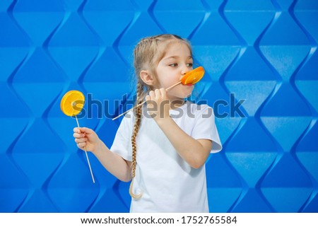 Little girl with a smile and pigtails, dressed in a white T-shirt, holds half an orange on hand, concept of a healthy lifestyle