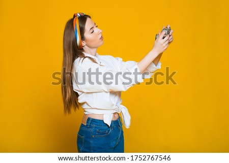 Attractive young woman standing isolated over yellow background, taking a picture with photo camera