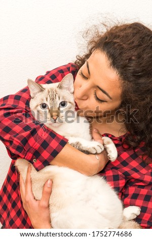 Lifestyle photo of a casual young Caucasian female who is holding, petting and kissing her cute gray stripped cat. Kitten enjoys being in girl's arms. Selective focus. Cat lover.
