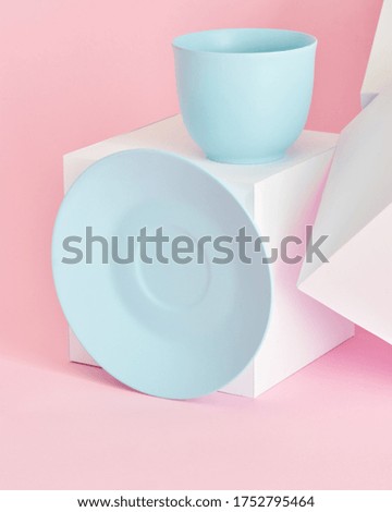 minimalism concept with light pastel colored blue cups and plate with white paper cubs on pink background. 