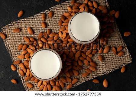 sprinkled almonds with glasses of milk on a dark black background, vegetarian milk without sugar and lactose, top view