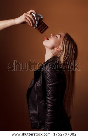 Hand with chocolate reaches for a beautiful girl. Girl with open mouth waiting for chocolate. Studio photography. Space for text. Copy space