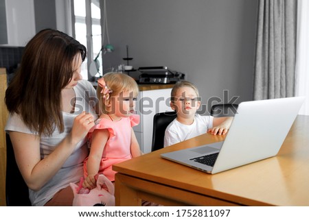 A mother with a young son and daughter watching educational programs on a laptop.