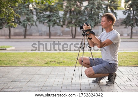 Young photographer shoots on digital SLR camera with a tripod in the park in summer