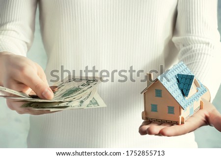 Real estate price and construction concept. Girl weighs money and a toy house in her hands