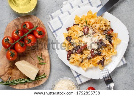 Pasta with sun-dried tomatoes and parmesan in a white plate on the table. Italian cuisine, ingredients and the finished dish, top view, flat lay
