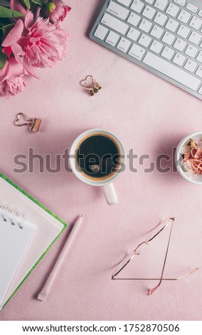 Pink office feminine desk workspace with pink peony, keyboard, cup of coffee, cosmetics, glasses, lipstick, empty notebook on white background. Flat lay, top view. Vertical photo