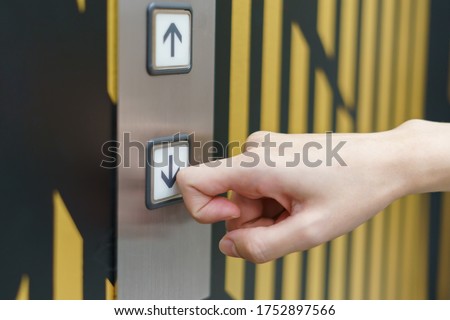 Woman finger pressing a down button of elevator button inside the building.  void direct contact during the outbreak of Covid-19.