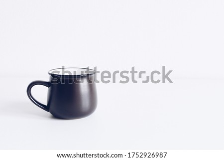 Enamel black mug on white table background mock up. Boho style classic stock photo. Still life composition with black ceramic cup. Hygge scene, product mockup template