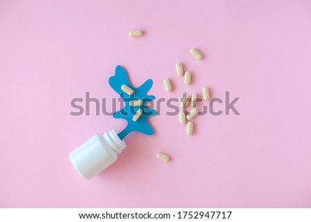 White pill packaging with blue paper splash on pink background. Medicine concept. 