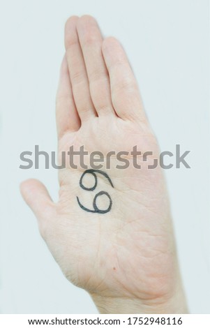 The palm of a young girl, top view, with a black felt-tip pen drawn the zodiac sign Cancer, on a light background. Features, characteristics of the sign Cancer in the palm of your hand, lines of fate,