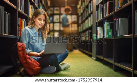 University Library: Gifted Beautiful Caucasian Girl Sitting On Floor, Uses Laptop, Writes Notes for Paper, Essay, Study for Class Assignment. Diverse Group of Students Learning, Studying for Exams.