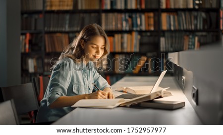 University Library: Beautiful Smart Caucasian Girl uses Laptop, Writes Notes for Paper, Essay, Study for Class Assignment. Focused Students Learning, Studying for College Exams. Side View Portrait Royalty-Free Stock Photo #1752957977