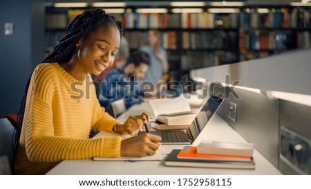 University Library: Gifted Black Girl uses Laptop, Writes Notes for the Paper, Essay, Study for Class Assignment. Diverse Multi-Ethnic Group of Students Learning, Studying for Exams, Talk in College Royalty-Free Stock Photo #1752958115