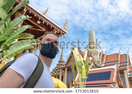 A caucasian man wearing a black face mask while walking around as a tourist visiting temples in Bangkok Thailand while Covid-19 situation started to ease Royalty-Free Stock Photo #1753013810