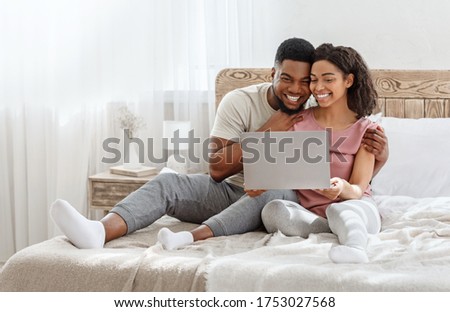 Couple in love watching photos on laptop while spending weekend together at home in bedroom, empty space