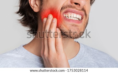 Tooth and gum inflammation. Guy suffers from pain in his mouth and presses hand to red sore spot, panorama, cropped, studio shot