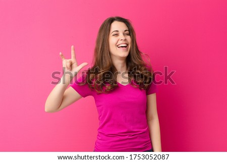 young pretty woman feeling happy, fun, confident, positive and rebellious, making rock or heavy metal sign with hand against pink wall