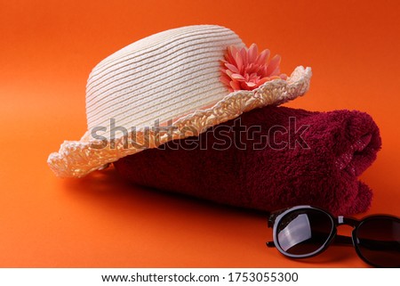close up shot of a light beige straw hat and beach things on the orange background, representing summer holidays concept