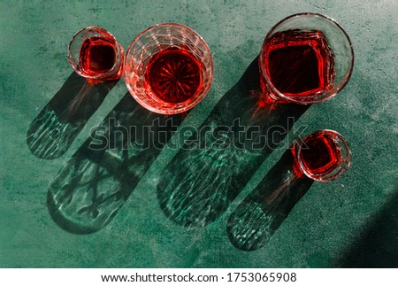 Creative beverage photography of red cocktail in different glasses under hard light over green background.